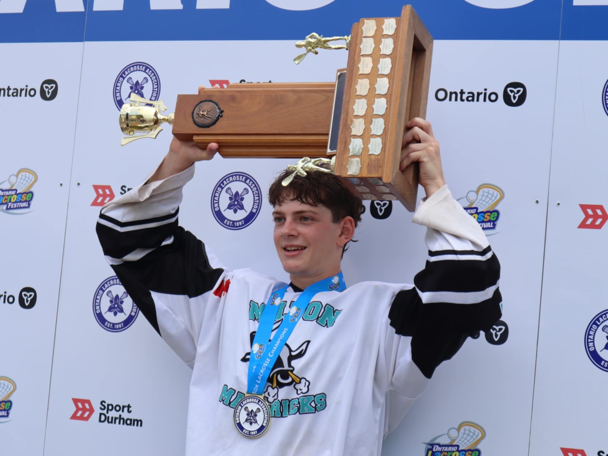 Jack Wilson holding up a lacrosse trophy in Milton Mavericks uniform